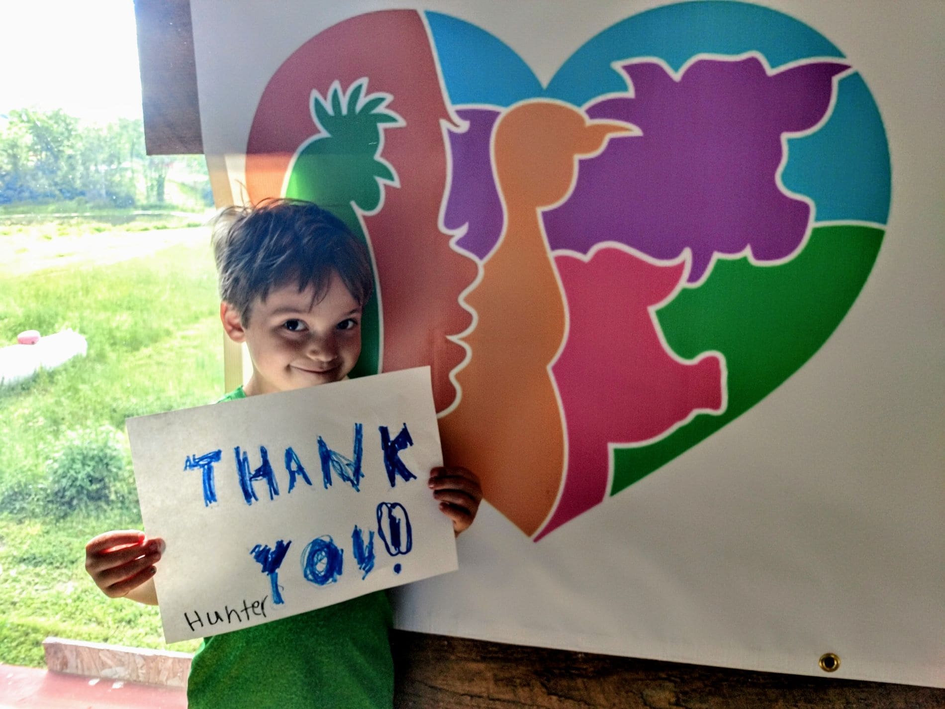 Kid with a thank you sign in front of Indraloka Animal Sanctuary logo poster