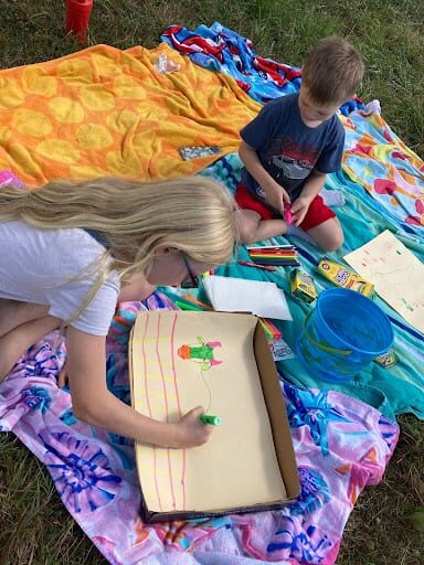 two kids on blankets on a meadow drawing and painting at Indraloka Animal Sanctuary